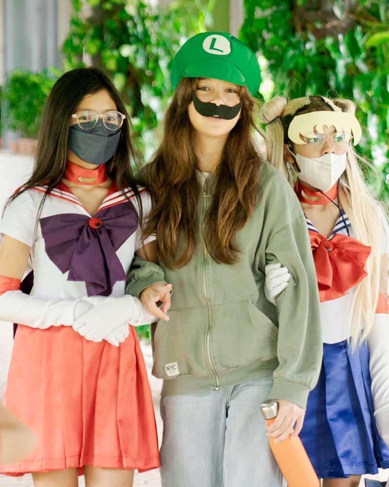 Three girls wearing masks and costumes are standing next to each other.