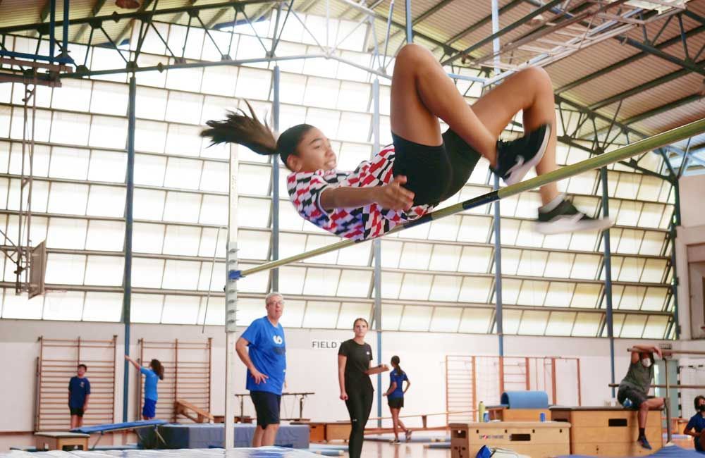 A young girl is jumping over a bar in a gym.