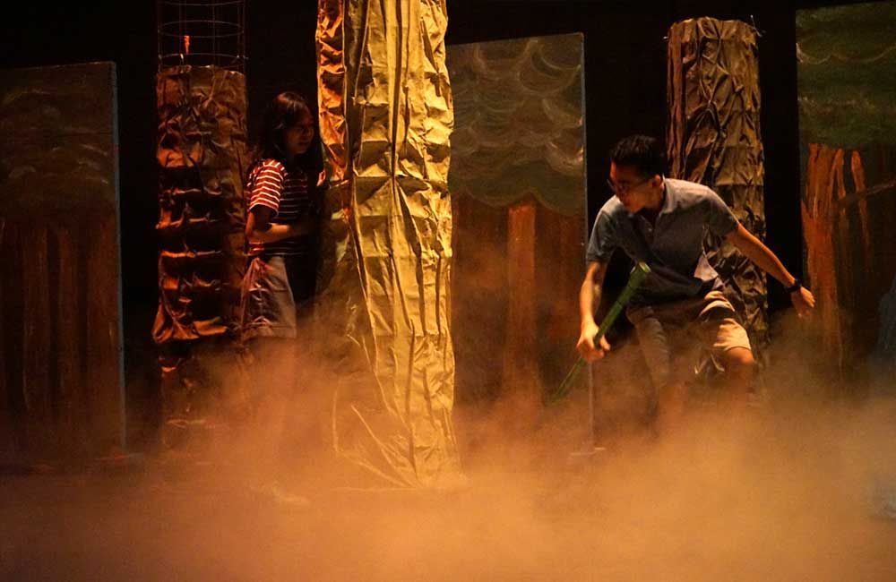 A man is standing on a stage in a foggy room holding a stick.