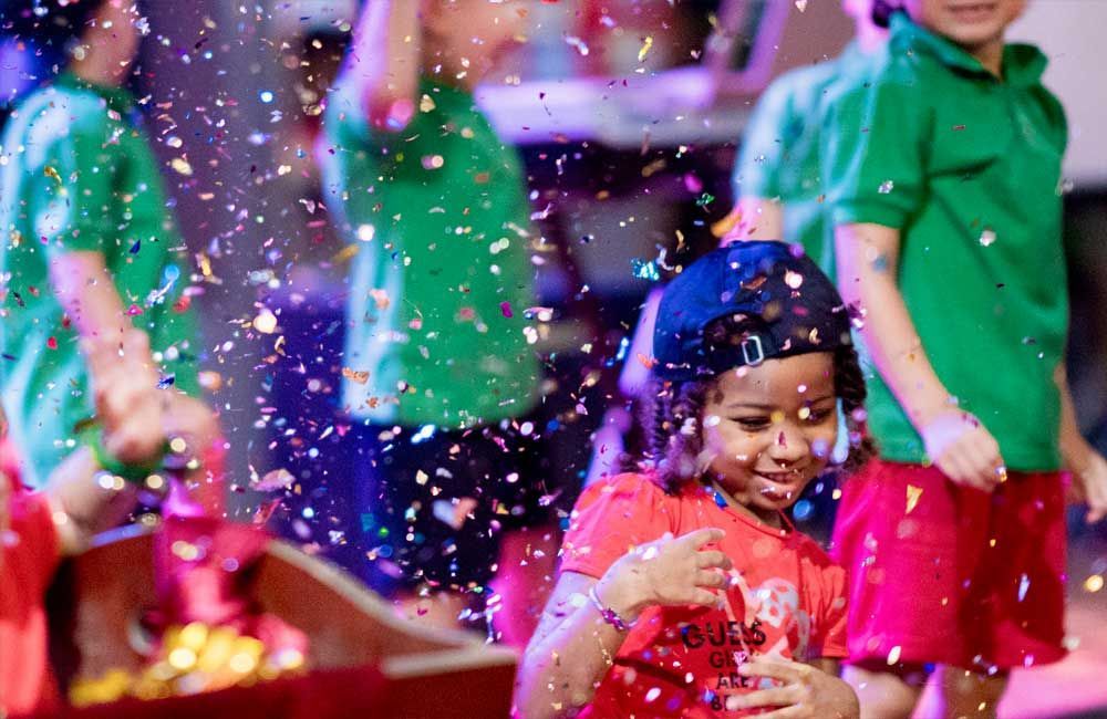 A group of children are playing with confetti on a stage.