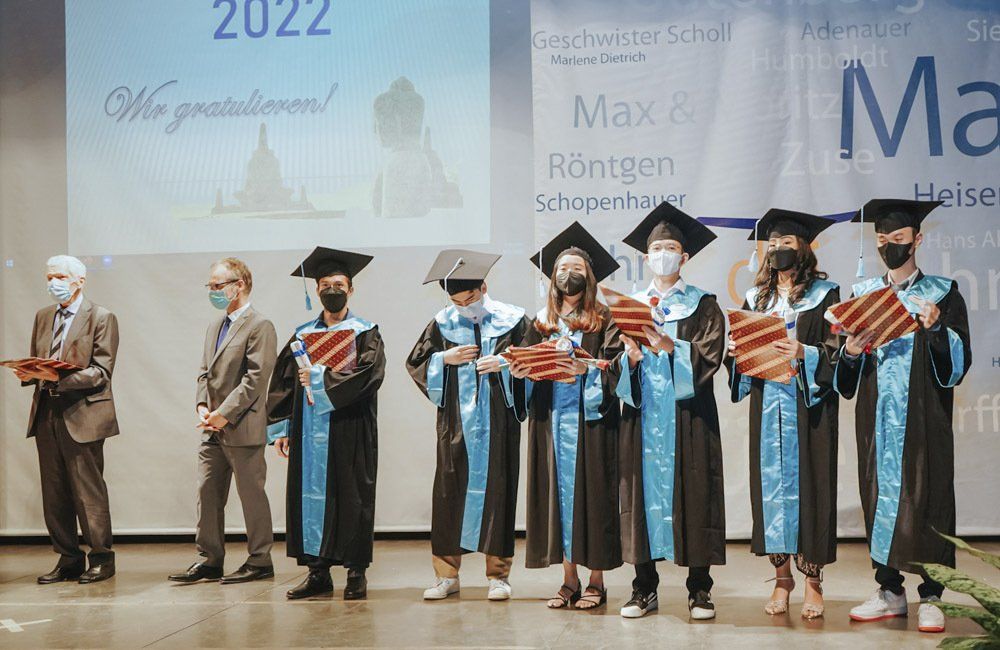 A group of graduates wearing masks and gowns are standing on a stage.