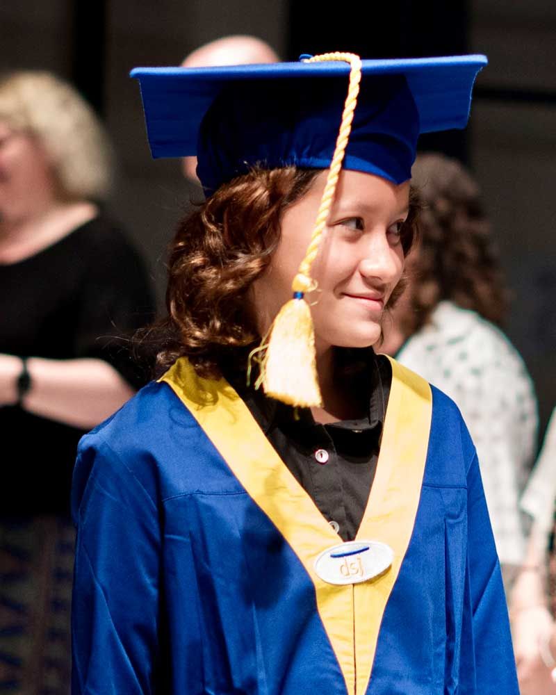 A young girl wearing a blue graduation cap and gown