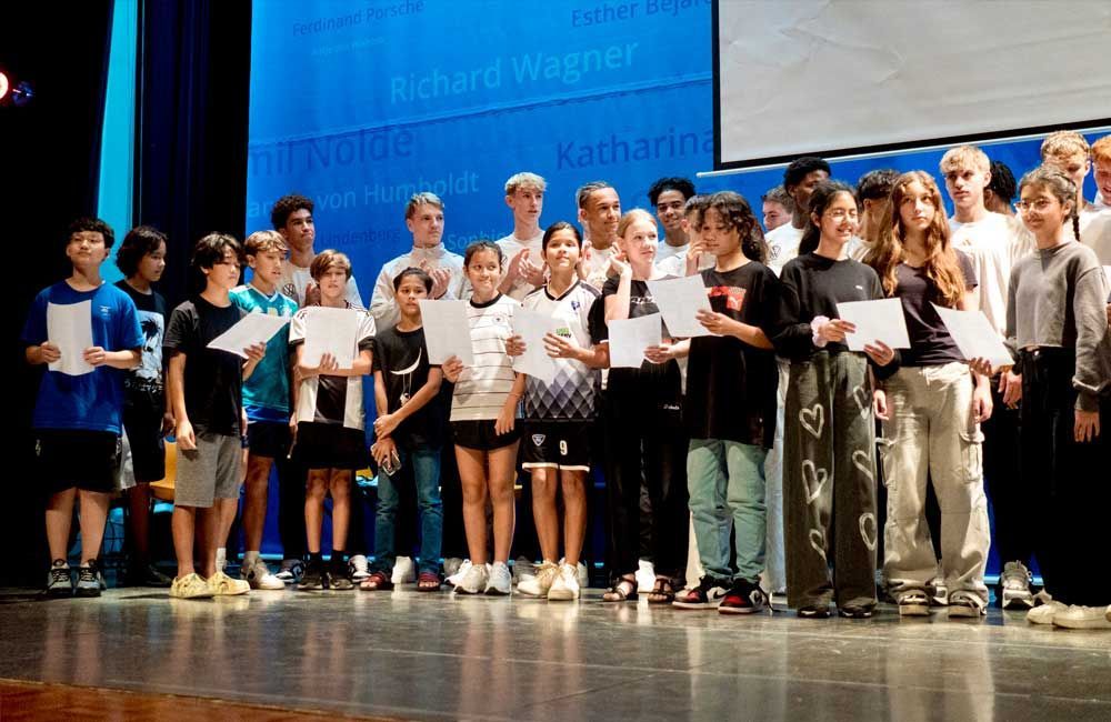 A group of children are standing on a stage holding papers.