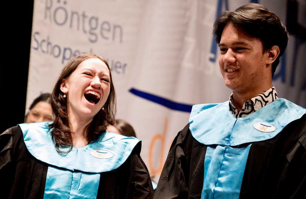 A man and a woman in graduation gowns are laughing together