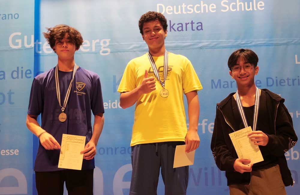Three young men are posing for a picture in front of a sign that says deutsche schule
