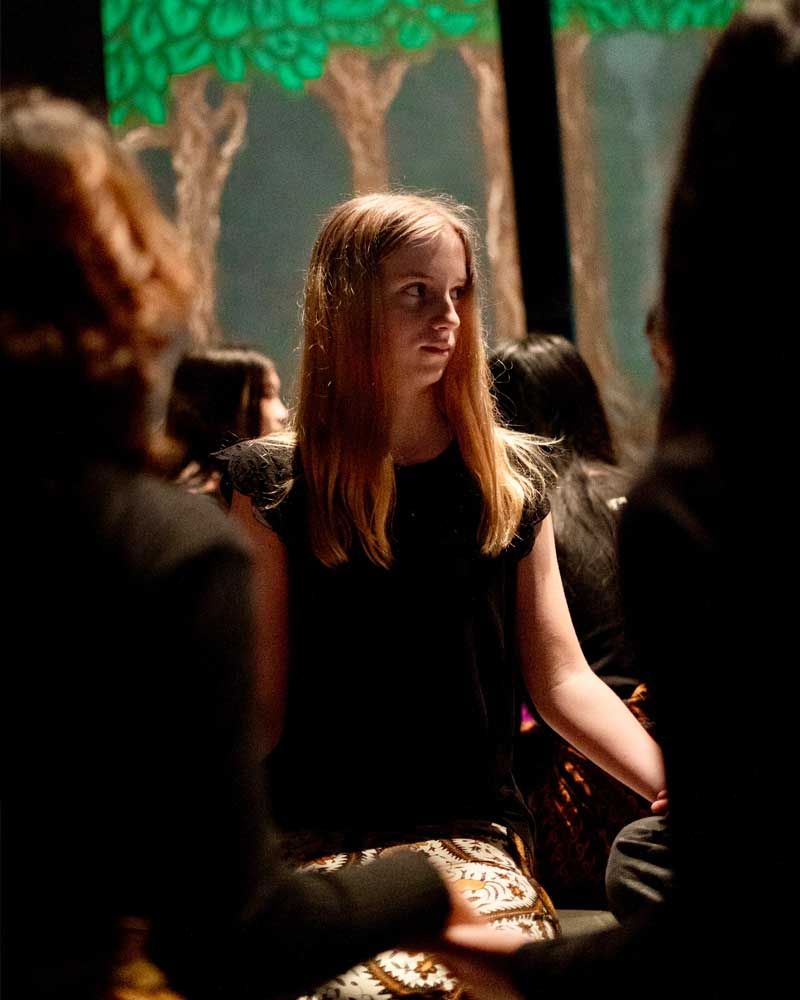 A woman in a black dress is sitting in a dark room with other people.