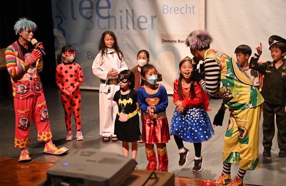 A group of children dressed in costumes are standing next to clowns on a stage.