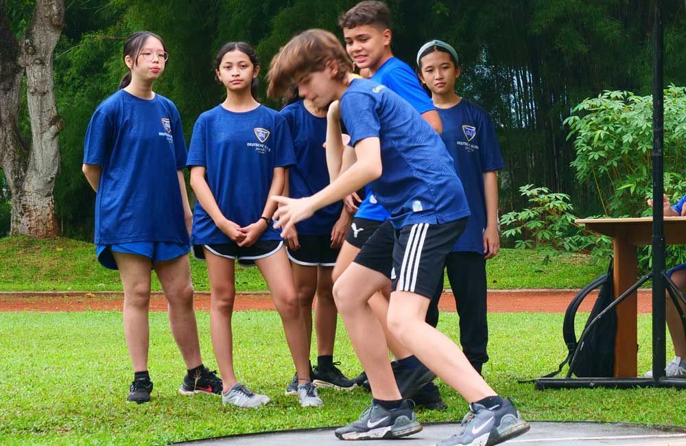A group of children are standing around a boy who is jumping in the air.