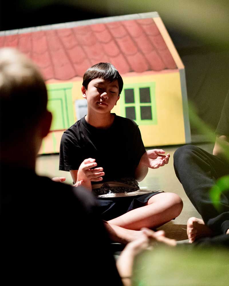 A boy sits on the floor in front of a toy house
