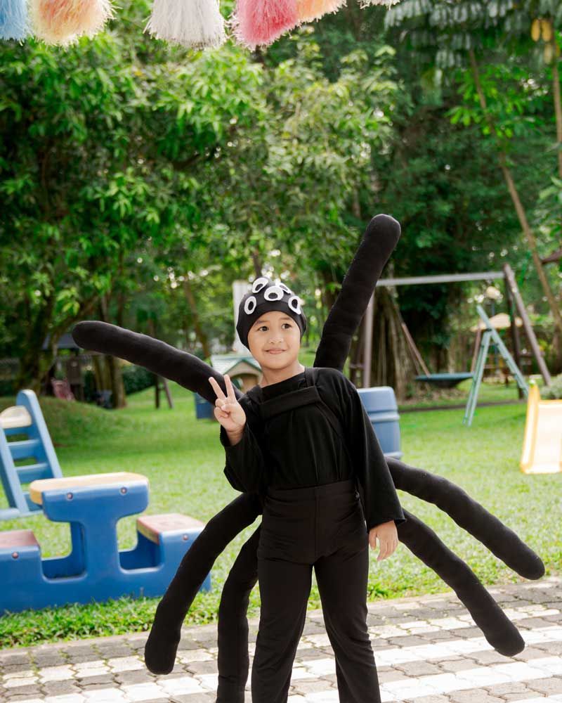 A little girl in a spider costume is giving a peace sign.