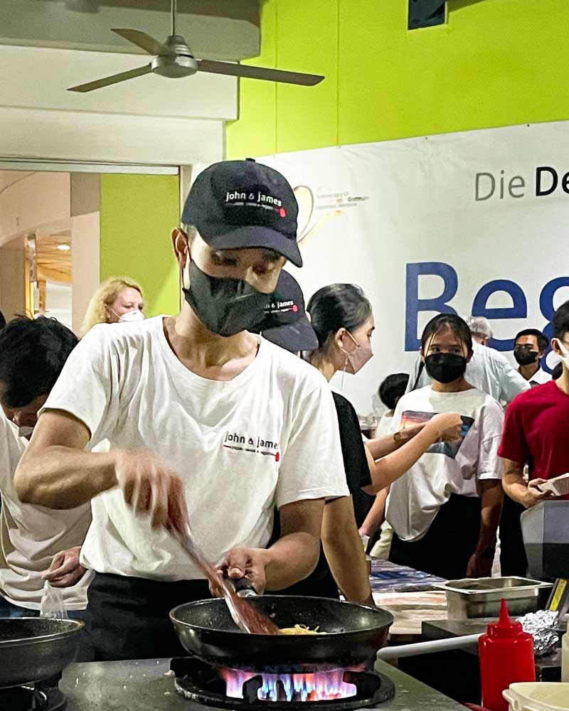 A man wearing a mask is cooking food in a kitchen.