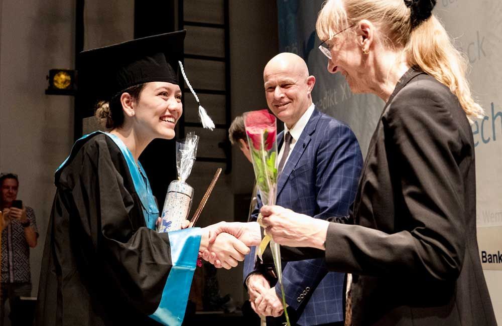 A woman in a graduation cap and gown is shaking hands with a man in a suit.