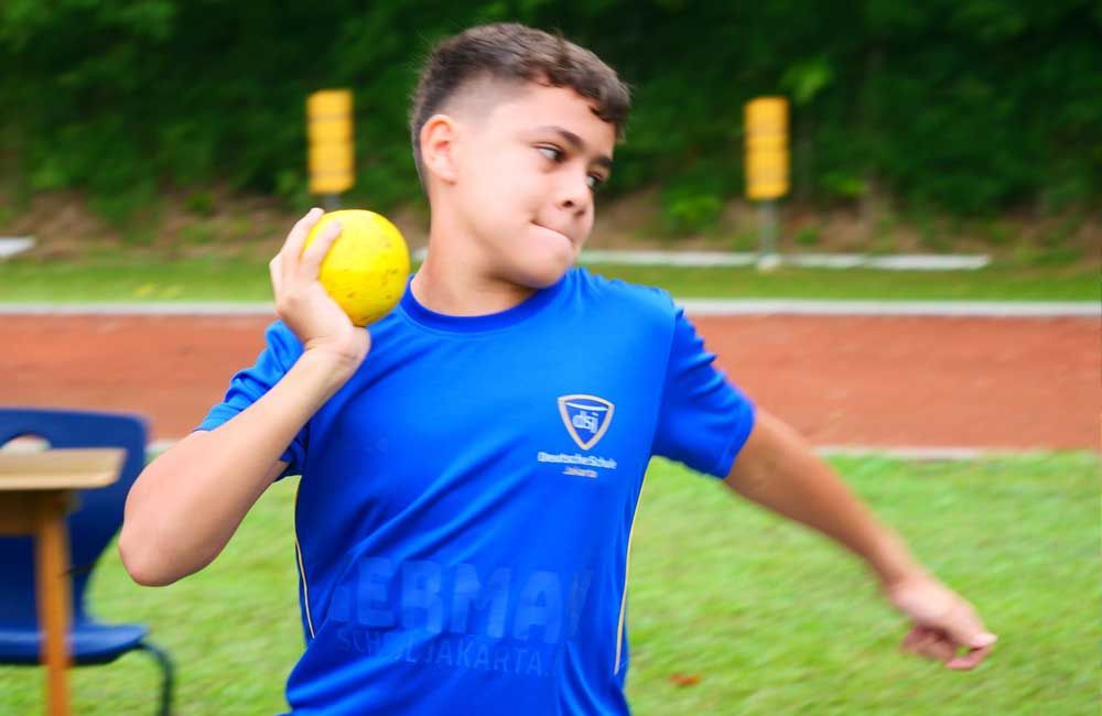A boy in a blue shirt is throwing a yellow ball.