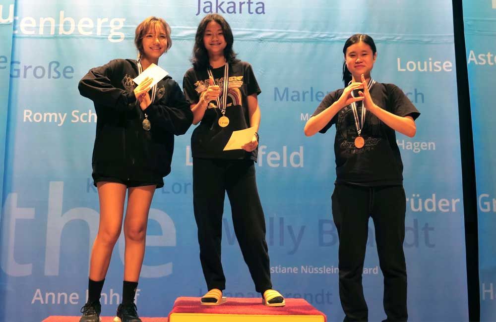 Three girls are standing on a podium in front of a wall that says jakarta