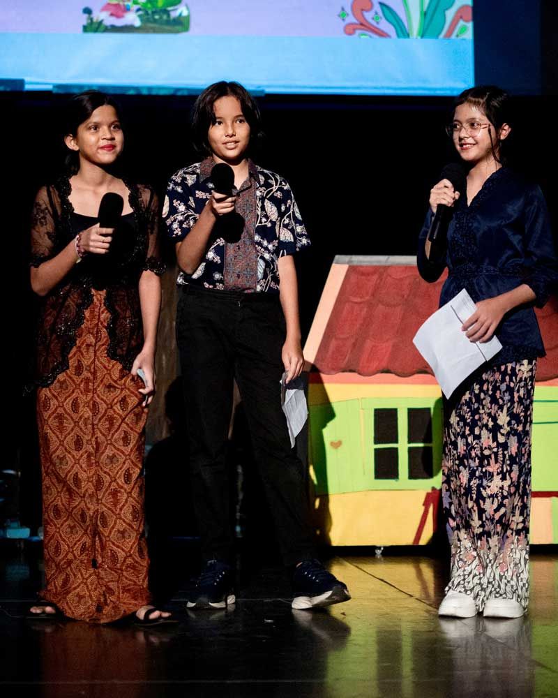 Three children are standing on a stage with microphones in their hands