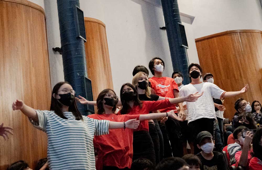A group of people wearing masks are standing in a room with their arms outstretched.