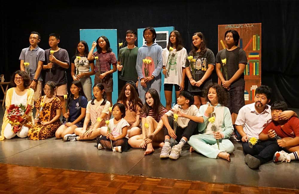 A group of children are sitting on the floor on a stage.
