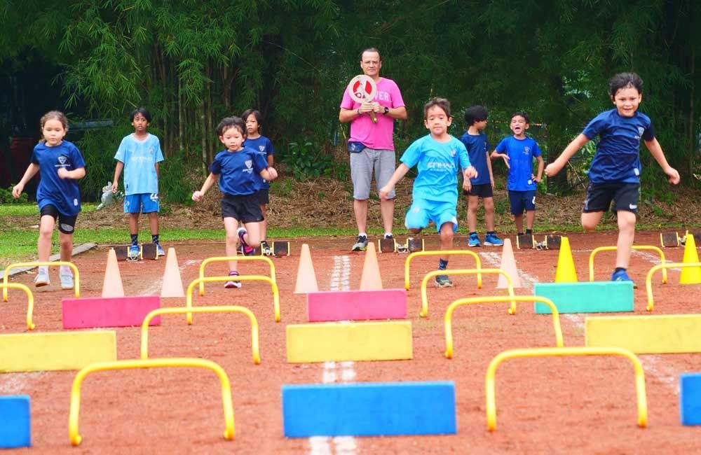 A group of children are running on a track with hurdles.