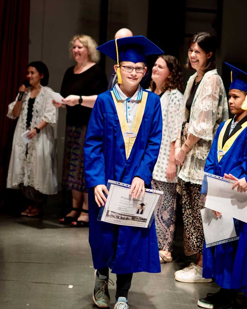 A boy in a blue graduation cap and gown is holding a certificate