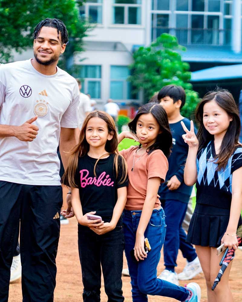A man in a barbie shirt is standing next to a group of children.