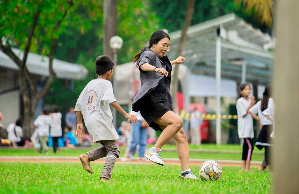 A woman and a boy are playing soccer in a park.