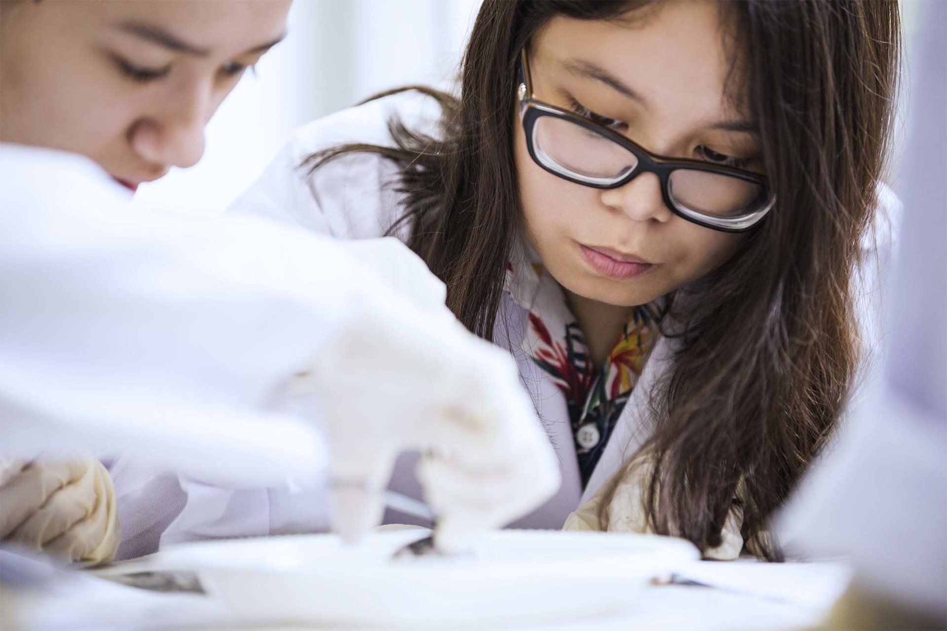 Two women in lab coats and glasses are working on a piece of paper.