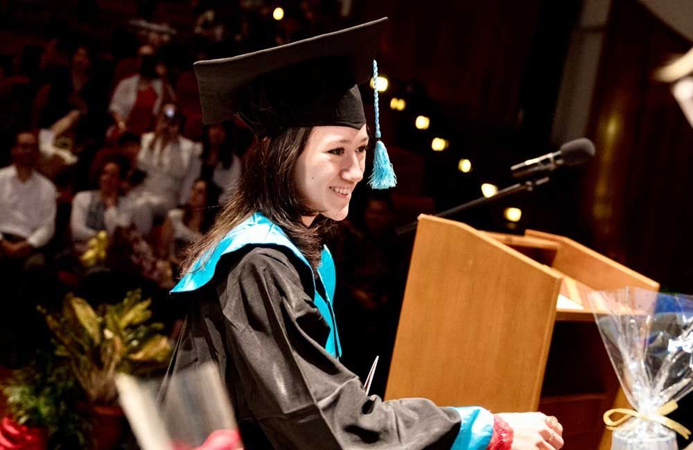 A woman in a graduation cap and gown is giving a speech at a podium.
