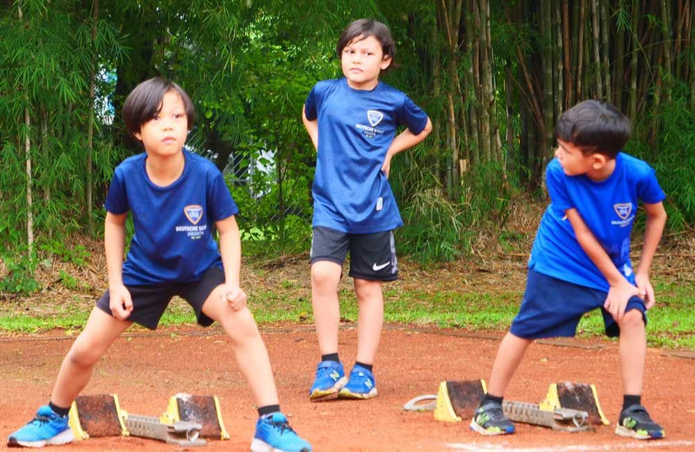 Three young boys in blue shirts are stretching on a track.