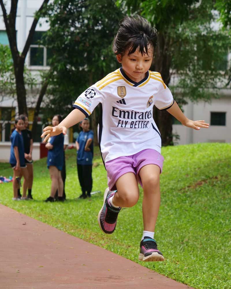 A young boy wearing an emirates fly better jersey is jumping in the air.