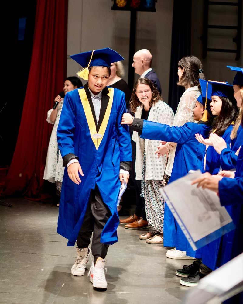 A man in a blue graduation cap and gown is walking down a stage.