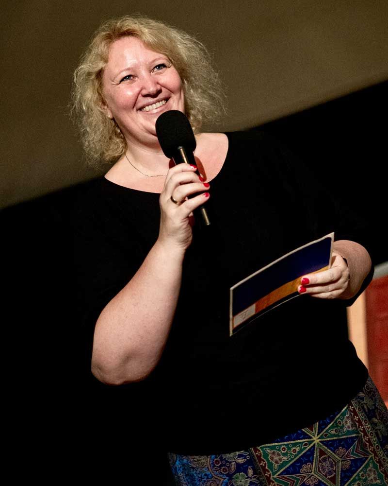A woman in a black shirt is holding a microphone and smiling