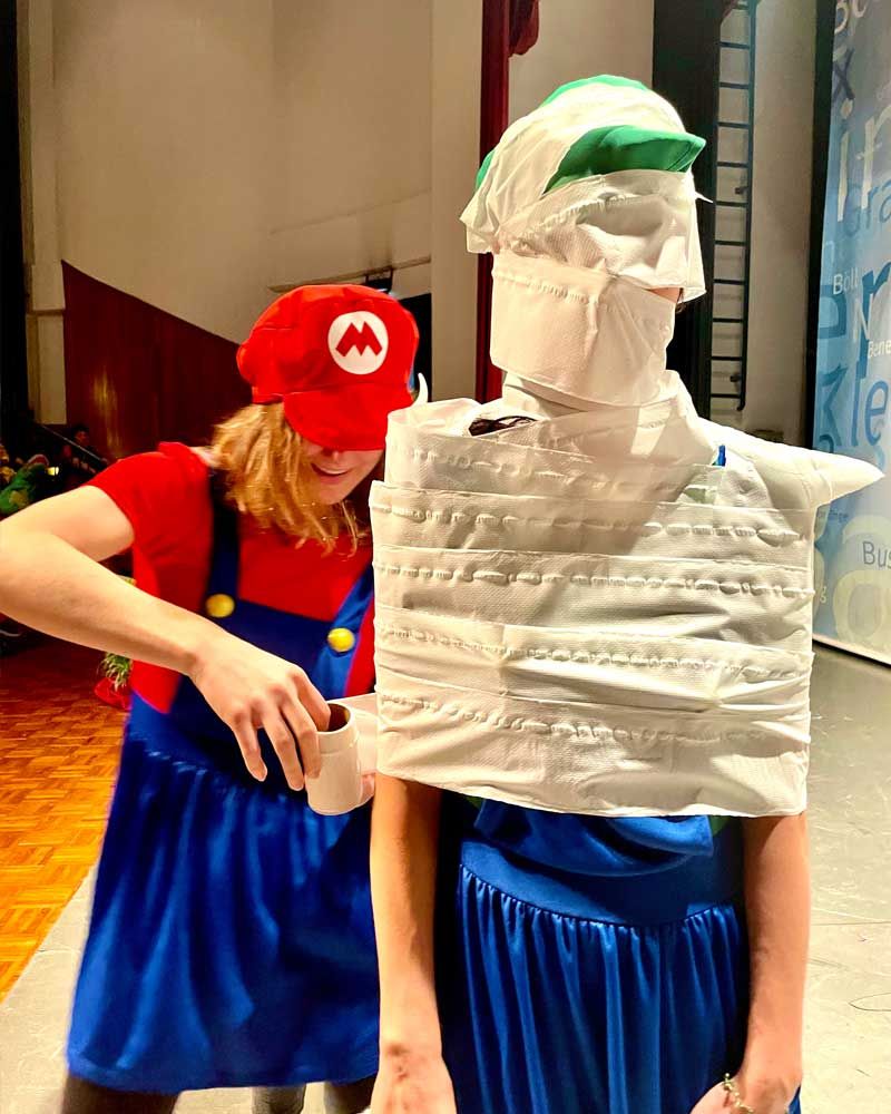 A woman in a mario costume is standing next to a man wrapped in toilet paper.