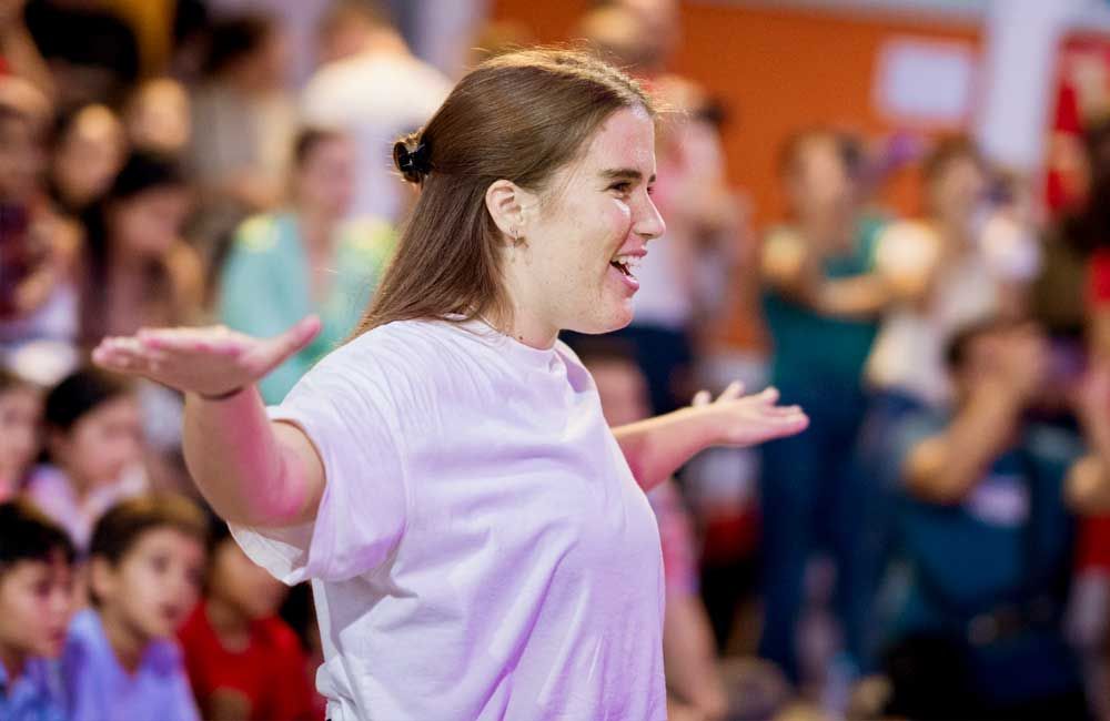 A woman is standing in front of a crowd of people with her arms outstretched.