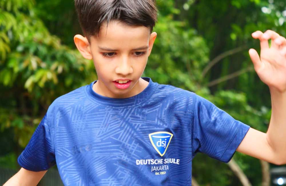 A young boy wearing a blue shirt with the word deutsche schule on it.