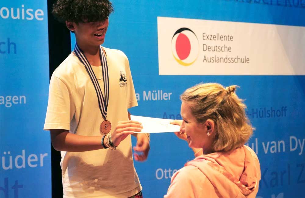 A boy wearing a medal is giving a certificate to a girl
