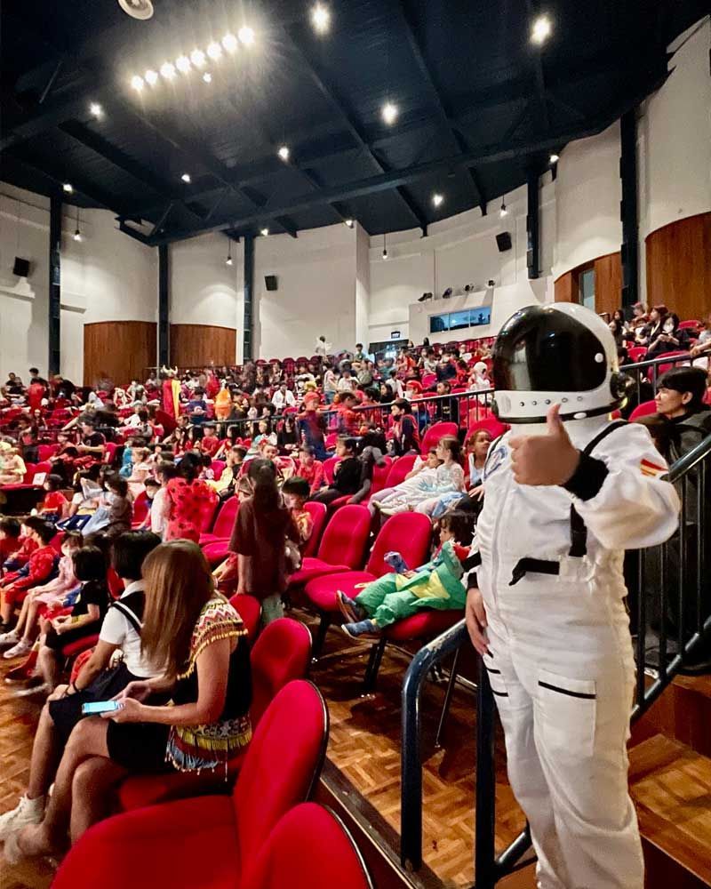 A man in an astronaut costume is standing in front of a crowd of people in an auditorium.