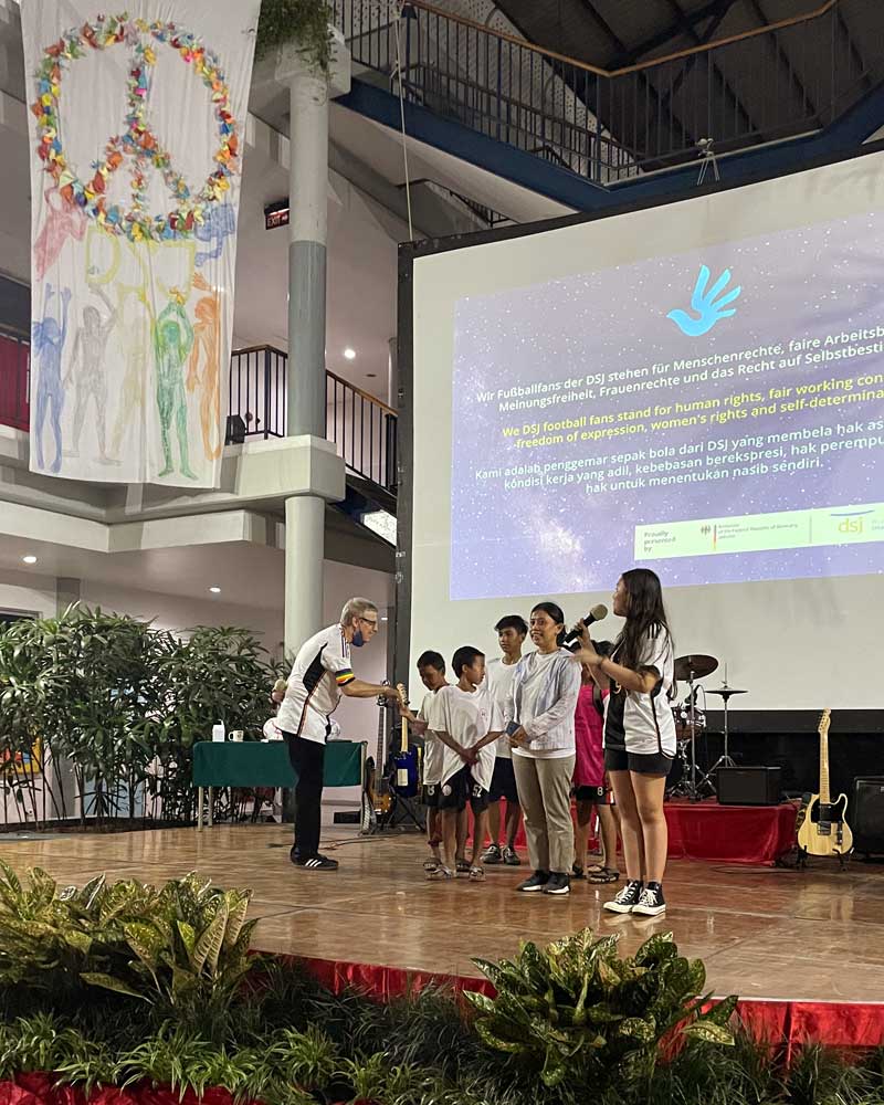 A group of children are standing on a stage in front of a large screen.