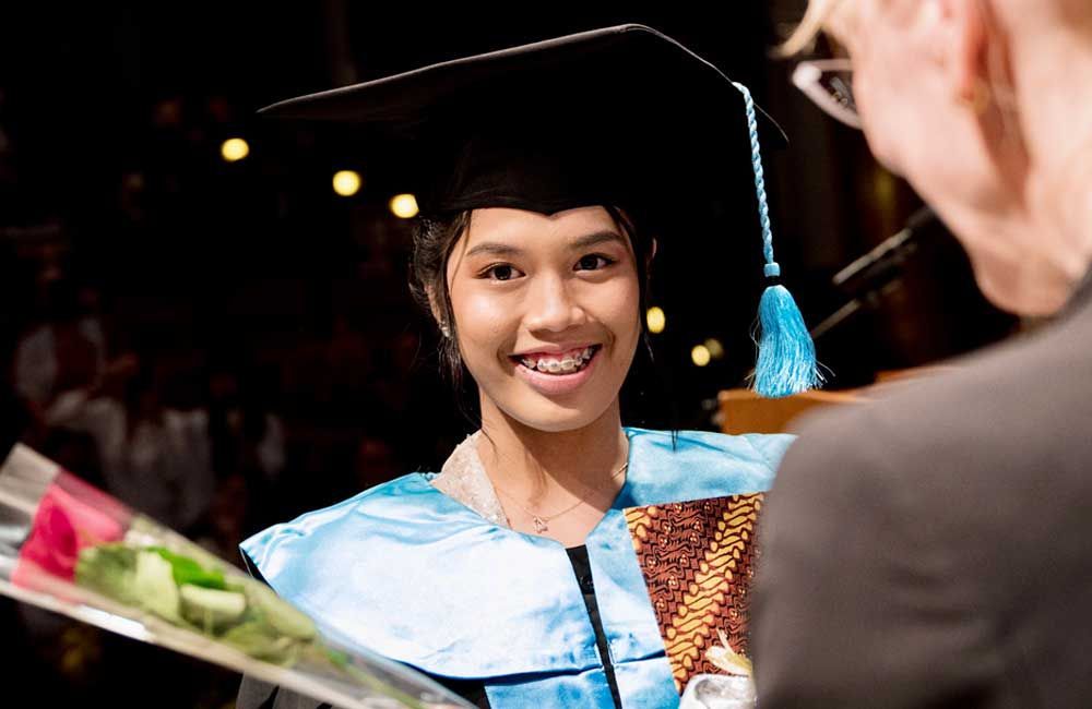 A woman in a graduation cap and gown is holding a bouquet of flowers.