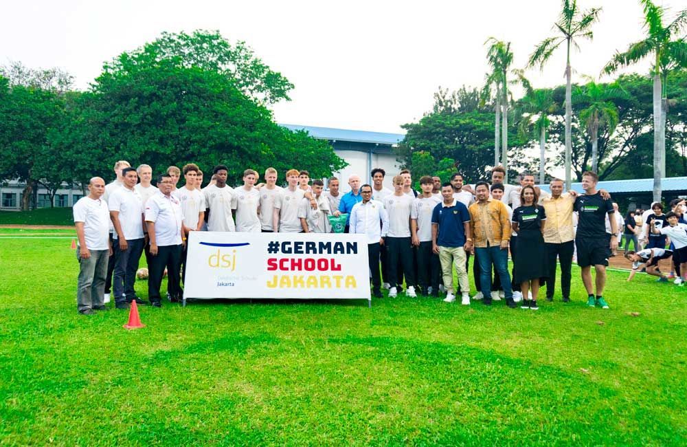A group of people standing in a field with a sign that says german school jakarta.