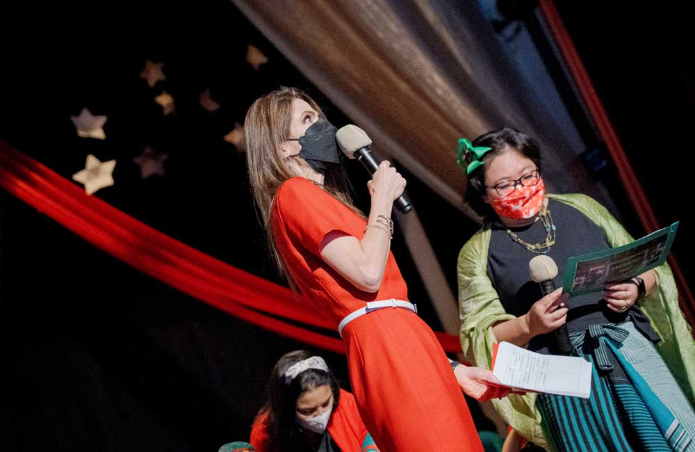 Two women wearing masks are standing on a stage holding microphones.