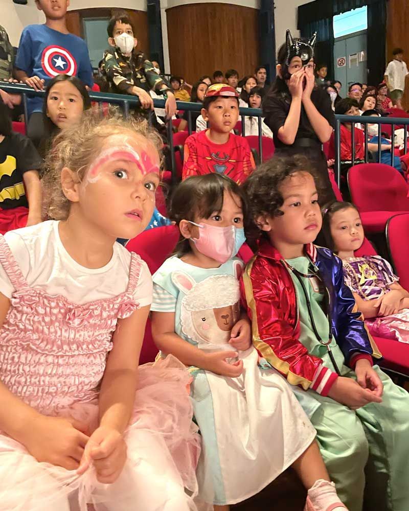 A group of children are sitting in a theater wearing masks.