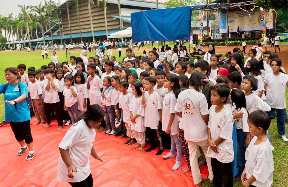 A large group of children are standing on a red tarp.