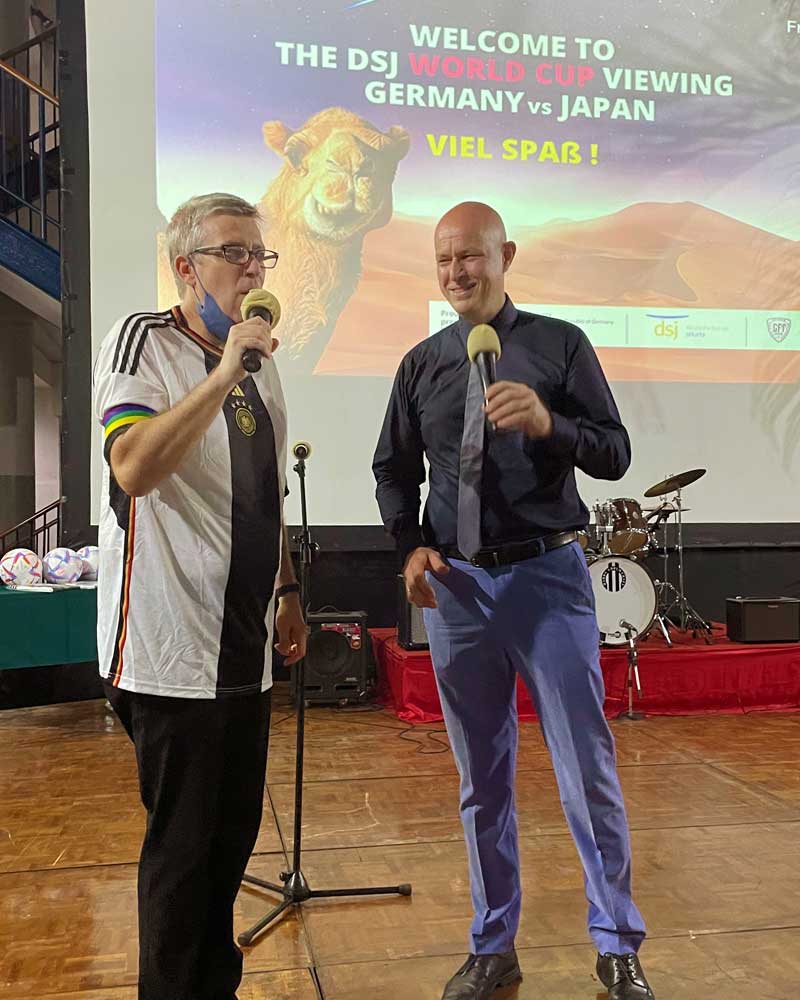 Two men are standing next to each other on a stage talking into microphones.