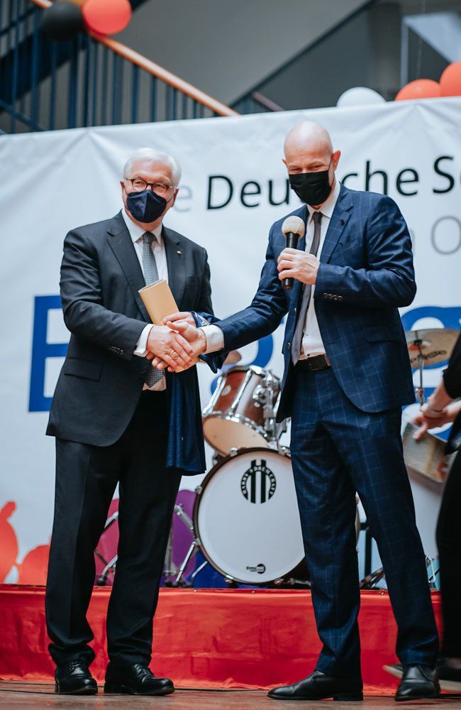 Two men wearing masks are shaking hands on a stage.