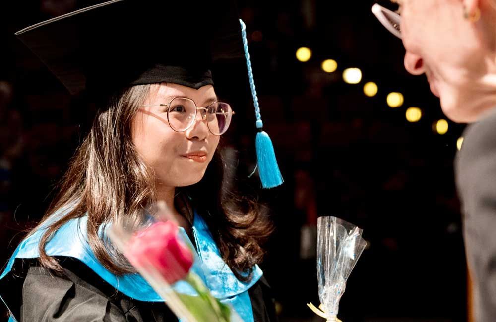 A woman in a graduation cap and gown is holding a bouquet of flowers.