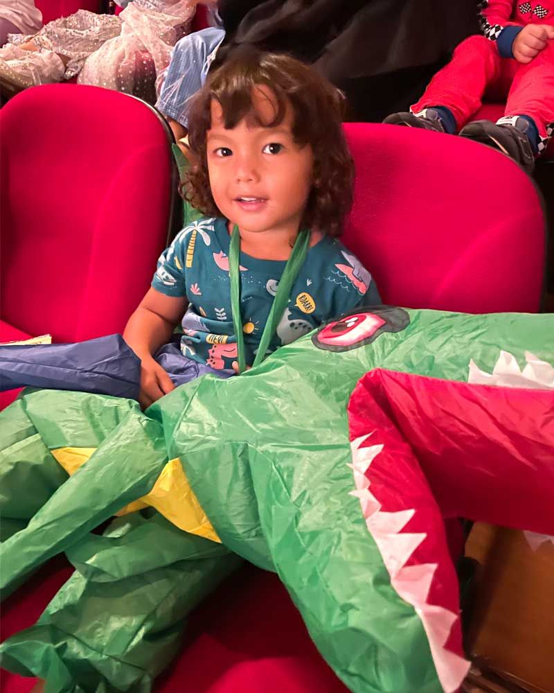 A little girl in a crocodile costume is sitting in a red chair.