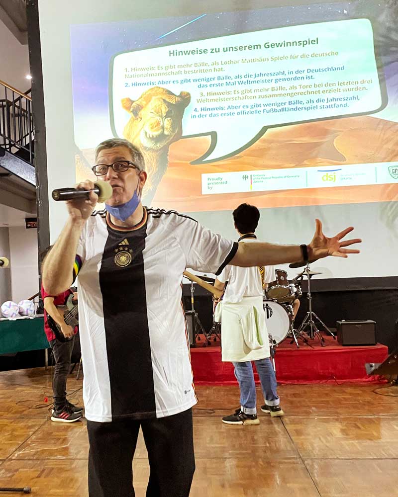 A man is singing into a microphone in front of a projector screen.