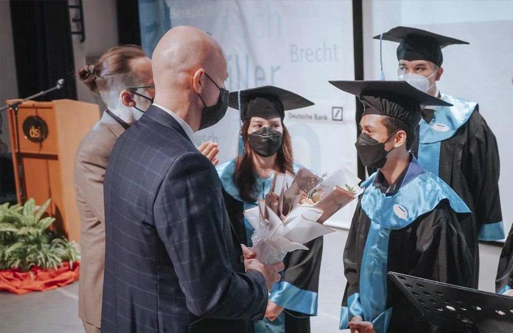 A group of graduates wearing masks are shaking hands with a man in a suit.