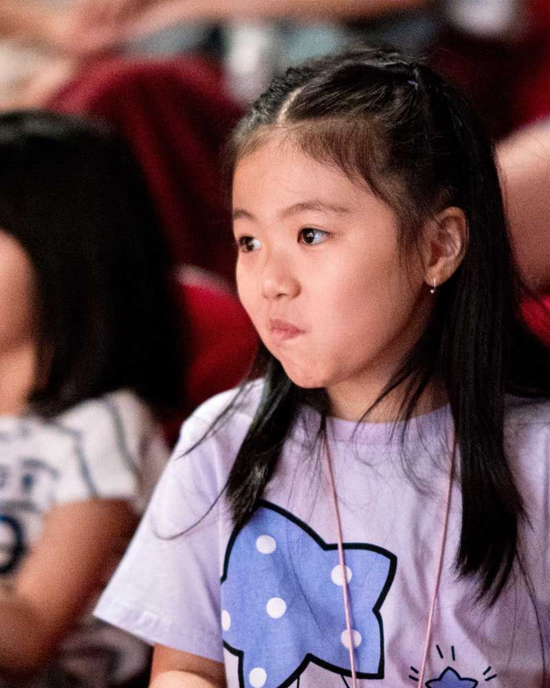 A little girl is sitting in a theatre wearing a hello kitty shirt.