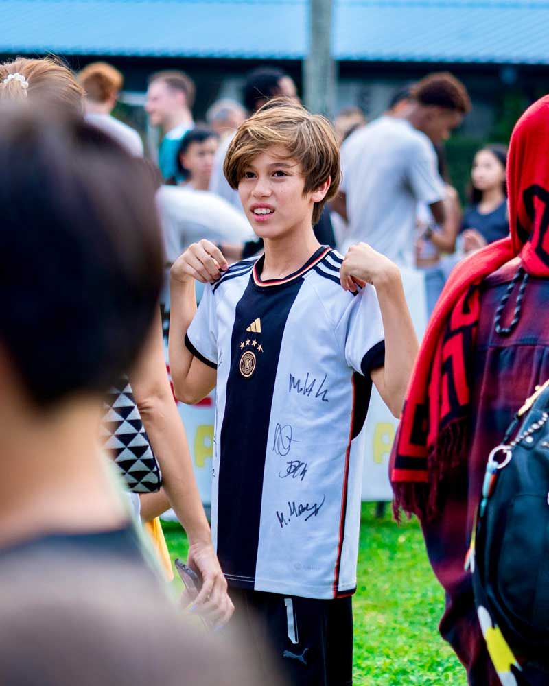 A young boy wearing a black and white striped shirt is standing in a crowd of people.